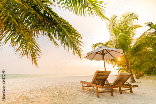 Tropical beach resort hotel background as summer landscape with lounge chairs and palm trees in sun rays and calm sea for beach banner. Luxury vacation and holiday destination concept