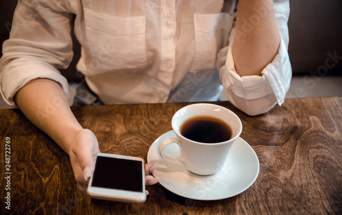 girl sits in a cafe and holds a cup of tea and a phone in her hands  waiting for a call