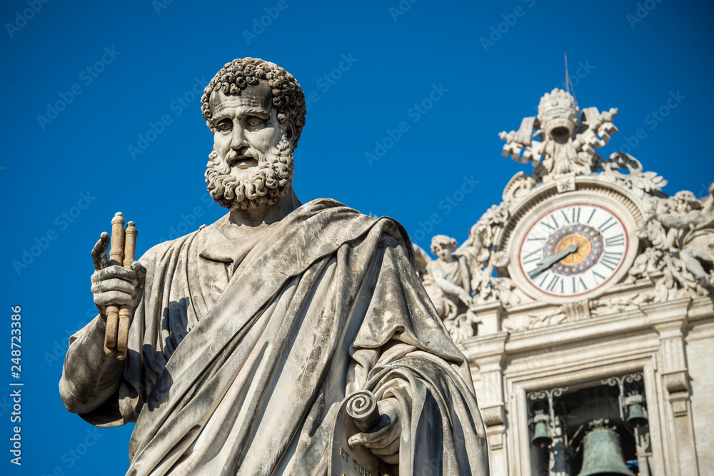 Fototapeta premium Vatican City, March 29, 2017: Statue of Saint Peter and Saint Peter's Basilica clock at background.
