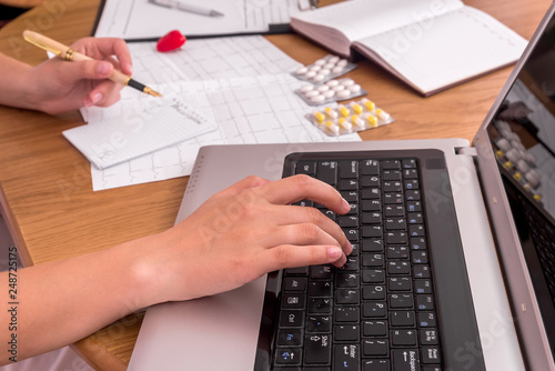 Doctor's hands typing on laptop and filling prescription