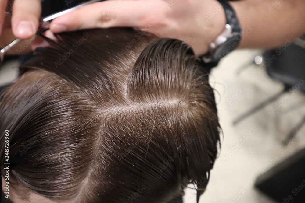 Fototapeta premium master hairdresser does hairstyle and style with scissors and comb. Master stacks hair of men in barbershop, hairdresser makes hairstyle for young man. Barber shop. Light 