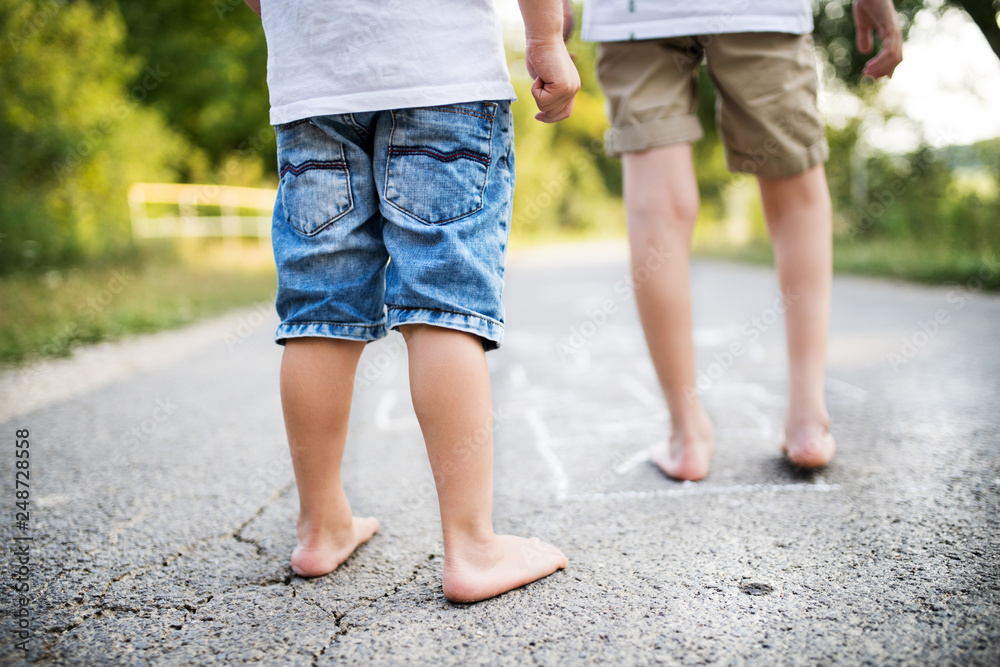 Obraz premium A rear view of two small boys hopscotching on a road in park on a summer day.