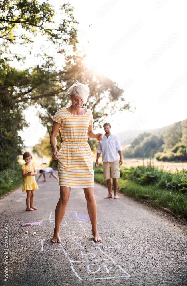 Obraz premium A young family with small children playing hopscotch on a road in summer.