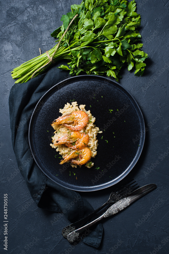 Italian risotto with shrimp on a black plate, a bunch of cilantro. Dark background, top view