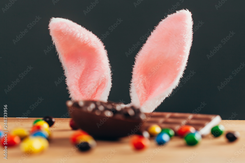 Easter concept. Rabbit ears behind chocolate easter egg on wooden table Easter concept. Rabbit ears behind chocolate easter egg on wooden table