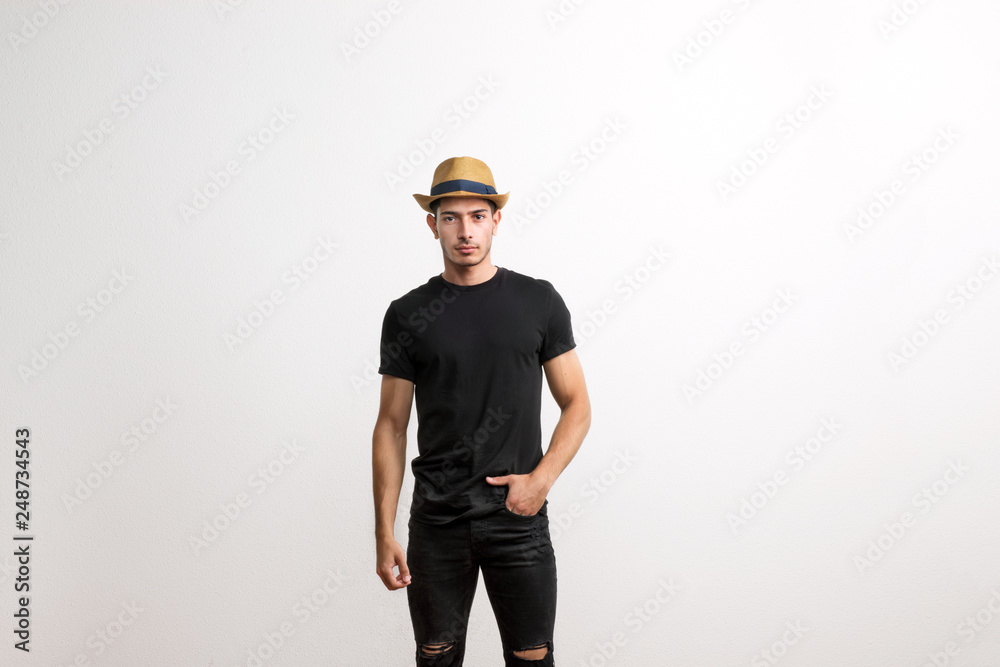A confident hispanic young man with hat and black T-shirt in a studio.