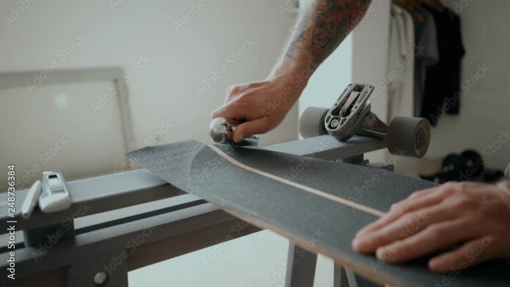 Skateboarder at home studio or workshop scrapes sides of board to prepare it for regripping and stick new tape. Concept diy and small nusiness owner or handmade process Skateboarder at home studio or workshop scrapes sides of board to prepare it for regripping and stick new tape. Concept diy and small nusiness owner or handmade process