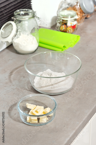 Przygotowanie składników do wypieku ciastek. Masło i mąka w szklanych pojemnikach stoją na kuchennym blacie. 