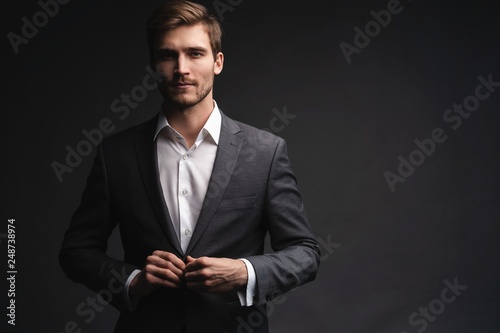 Portrait of serious handsome man in gray suit buttoning jacket