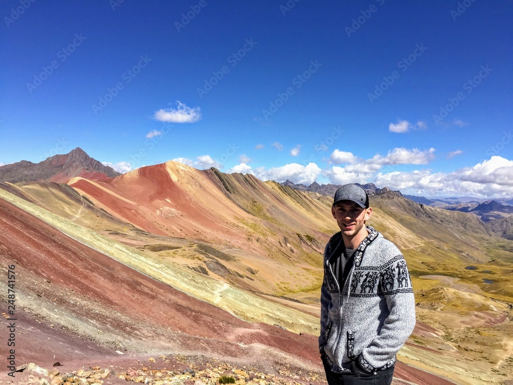A young male tourist enjoying the view of the incredible Rainbow Mountains outside of Cusco, Peru.  The amounts are a variety of colours from the 