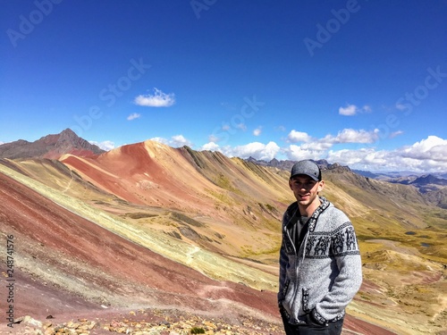 A young male tourist enjoying the view of the incredible Rainbow Mountains outside of Cusco, Peru.  The amounts are a variety of colours from the  © christopher
