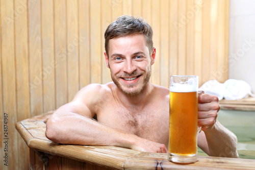 Męski relaks. Przystojny mężczyzna zażywa kąpieli w bali z woda termalną pijąc piwo kuflowe.