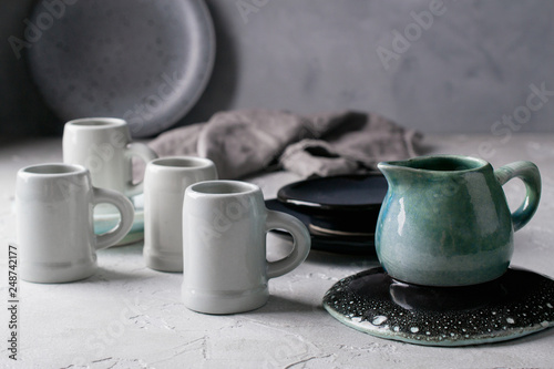 Set of grey rustic coffee cup handcraft and blue ceramic cream jug against shabby grey wall. Natural  handmade crockery tableware