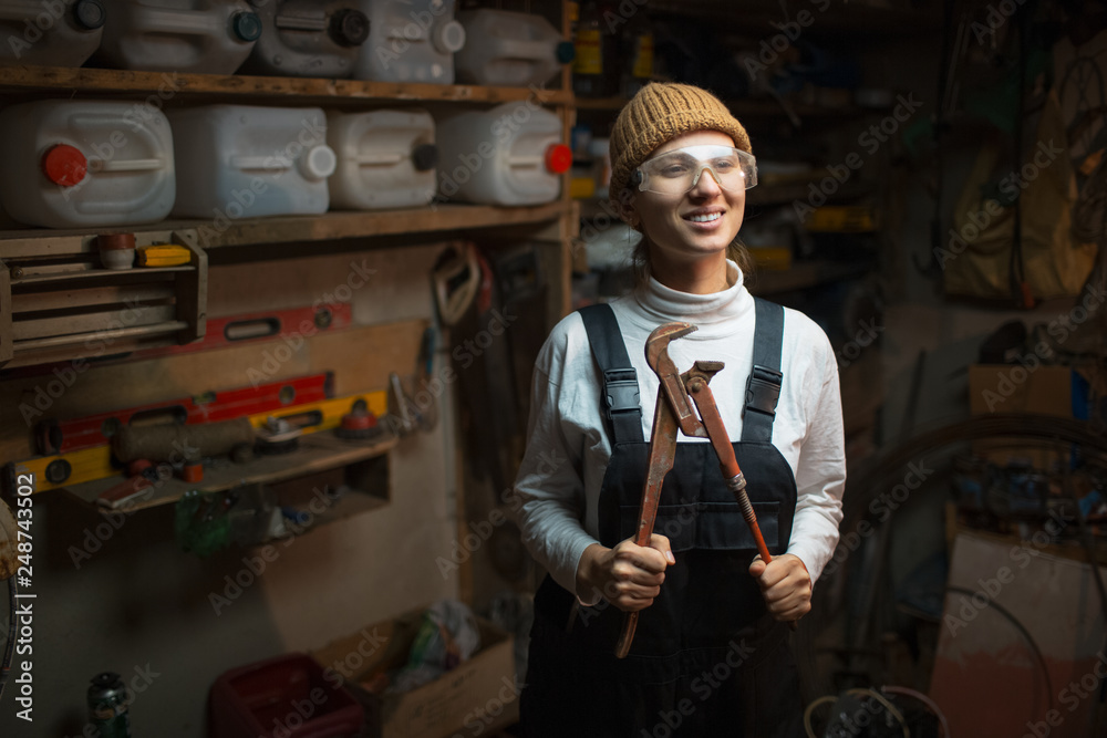 Portrait of smiling young builder girl standing in old workshop room, wearing construction glasses. Portrait of smiling young builder girl standing in old workshop room, wearing construction glasses.