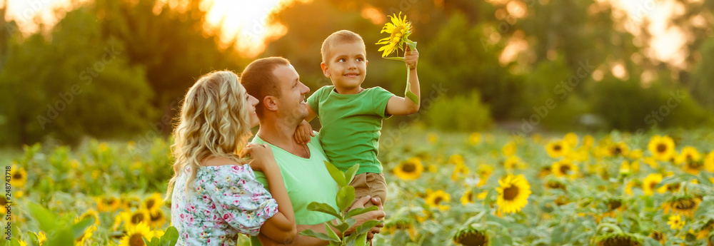 Happy family having fun in the field of sunflowers. Father hugs his son. Mother holding sunflower. outdoor shot - obrazy, fototapety, plakaty 