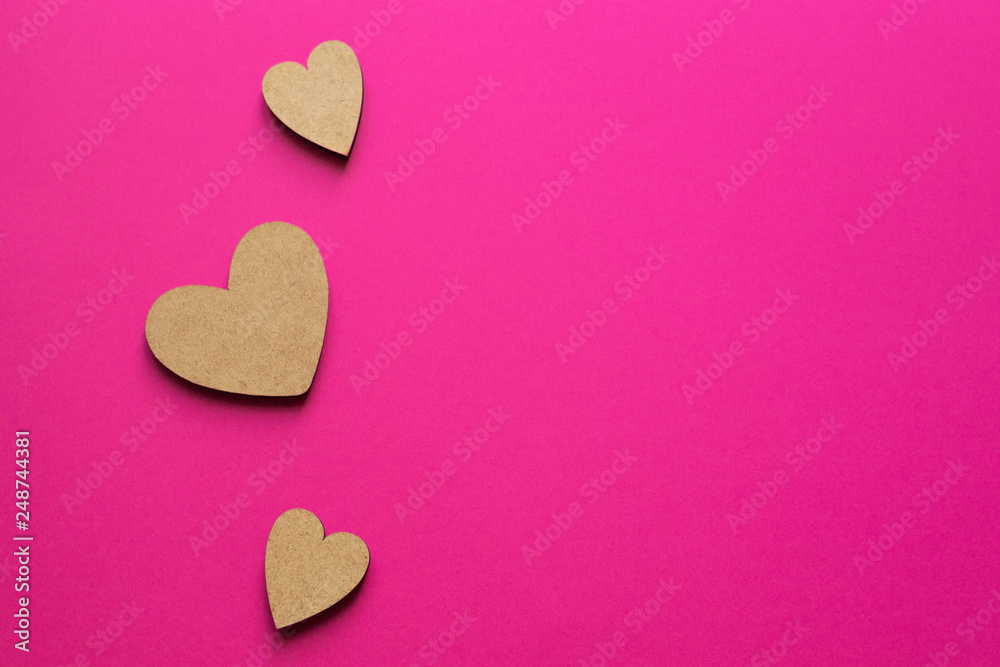 Obraz premium Little wooden hearts on pink background. Romantic composition with copy space for greeting.