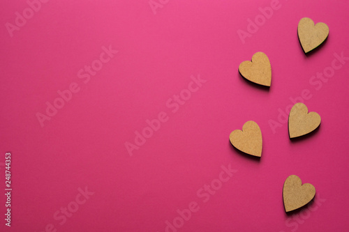 Little wooden hearts on pink background. Romantic composition with copy space for greeting.