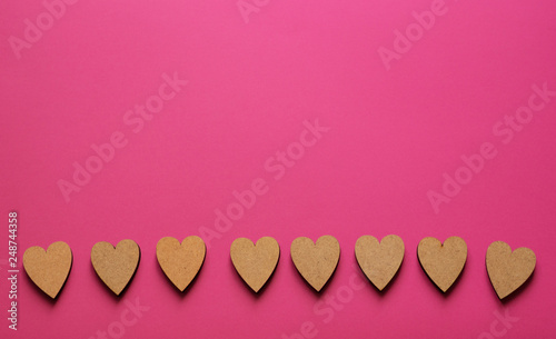Line of little wooden hearts on pink background with copyspace. Love flatlay from top view.