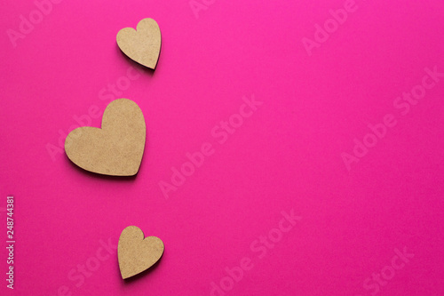 Little wooden hearts on pink background. Romantic composition with copy space for greeting.