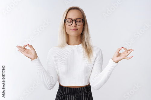 Female entrepreneur having break meditation to release negativity and bad emotions practicing yoga breathing deep with closed eyes and patient relaxed smile standing in lotus pose with mudra gesture