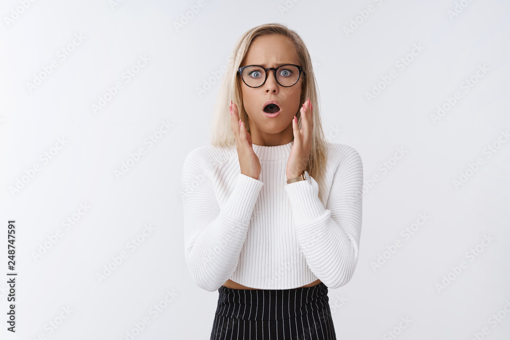 Blond woman in shock standing in stupor speechless from devestation being witness of terrible accident raising hands in fright and worry open mouth and frowning shook over white background