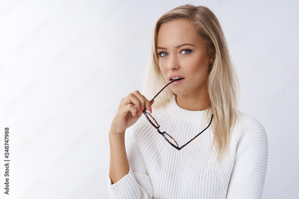 Close-up shot of focused and thoughtful attractive sensual young blond female employee in elegant sweater bite frame glasses and gazing at camera deep, thinking posing serious over white background Close-up shot of focused and thoughtful attractive sensual young blond female employee in elegant sweater bite frame glasses and gazing at camera deep, thinking posing serious over white background