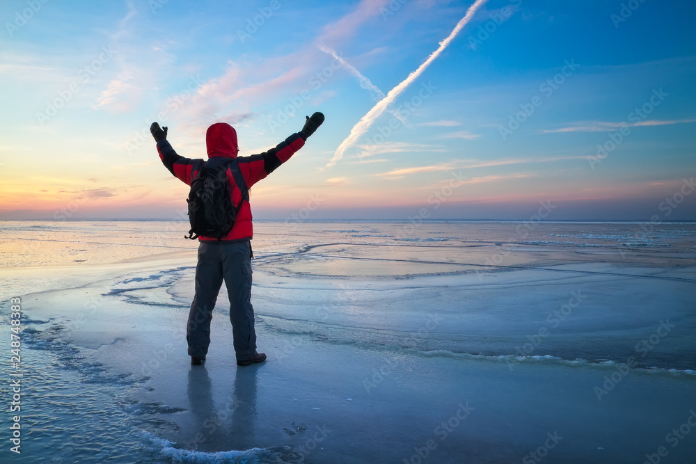 Fototapeta premium Nature photographer traveler on the frozen lake during sunrise in winter. Beautiful colorful landscape with people
