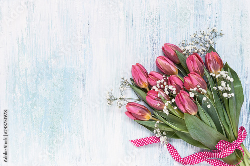 Pink tulips and gypsophila flowers decorated with ribbon on blue background. Top view, copy space.