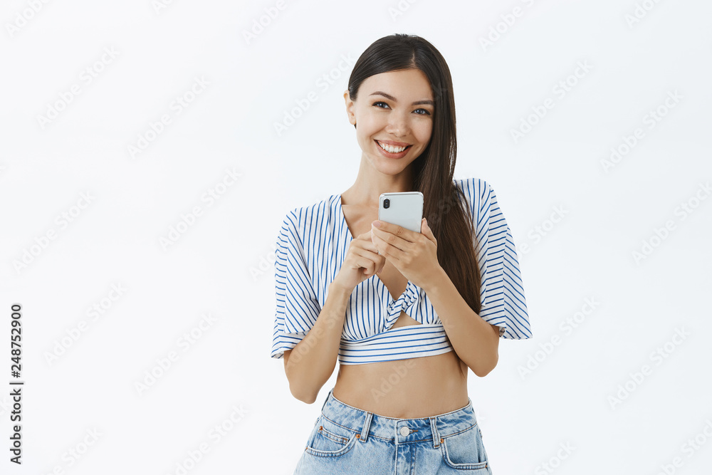 Portrait of silly and joyful charming asian woman in cropped blouse holding smartphone close to chest smiling and laughing from joy and happiness receiving device as gift over white background Portrait of silly and joyful charming asian woman in cropped blouse holding smartphone close to chest smiling and laughing from joy and happiness receiving device as gift over white background