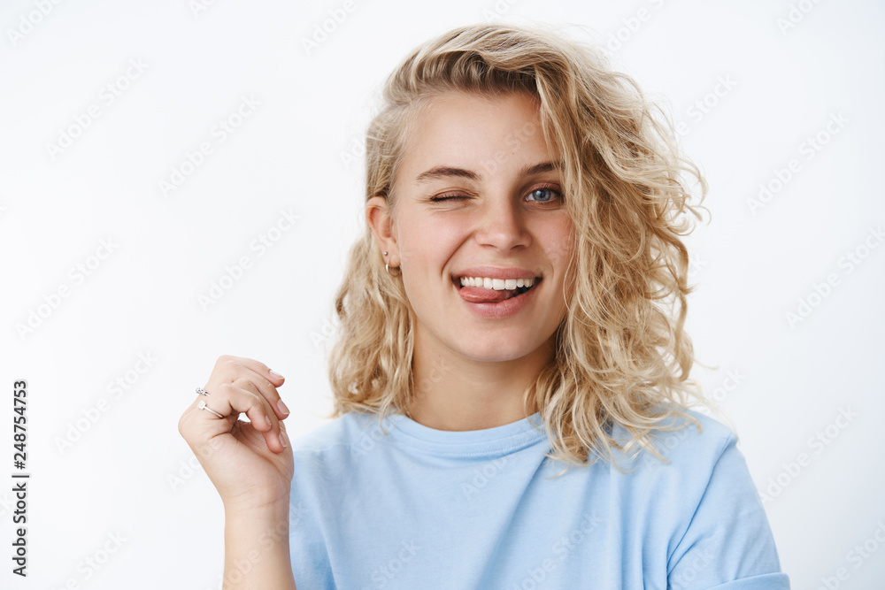 Obraz premium Girl in flirty and happy mood winking and sticking out tongue playfully at camera as posing over white background, smiling having fun and enjoying life, leading carefree lifestyle over white wall