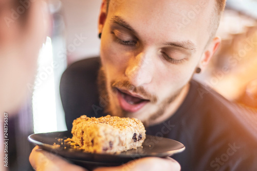 A stylish young man, a hipster, with a beard seductively stretches to the pie, trying to bite him. concept of an appetizing dish, a dessert, a cake that you want to eat
