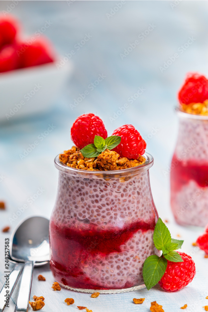 Served glass jars filled with delicious chia pudding with raspberry and crunchy granola on top Served glass jars filled with delicious chia pudding with raspberry and crunchy granola on top