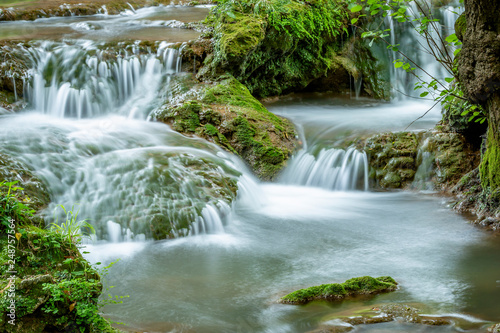Fototapeta Naklejka Na Ścianę i Meble -  Panoramic view of small waterfalls streaming into small pond in green forest in long exposure 