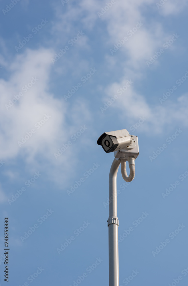 A cantilevered modern white security CCTV camera, pointing and checking to all coming visitors in a modern house’s front gate during the day. A cantilevered modern white security CCTV camera, pointing and checking to all coming visitors in a modern house’s front gate during the day.