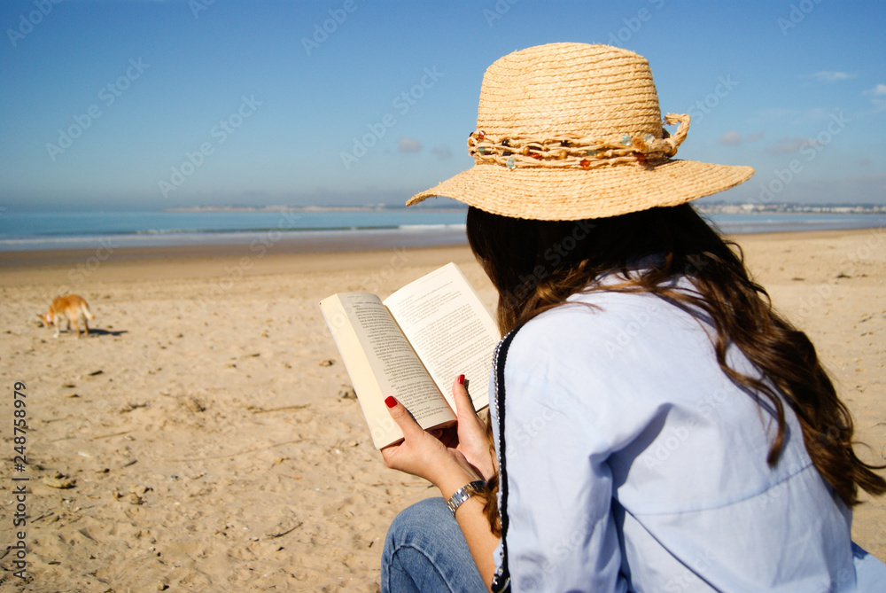 Young woman reading a book on the beach in winter sunny day