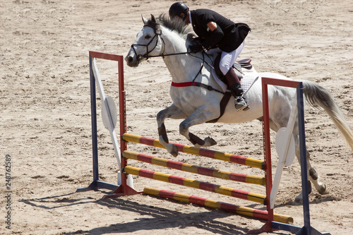 A man on the horseback of a white horse jumping the hurdles