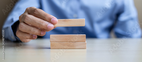 Businessman hand holding wooden building blocks on table background. Business planning, Risk Management, Solution and strategy Concepts photo
