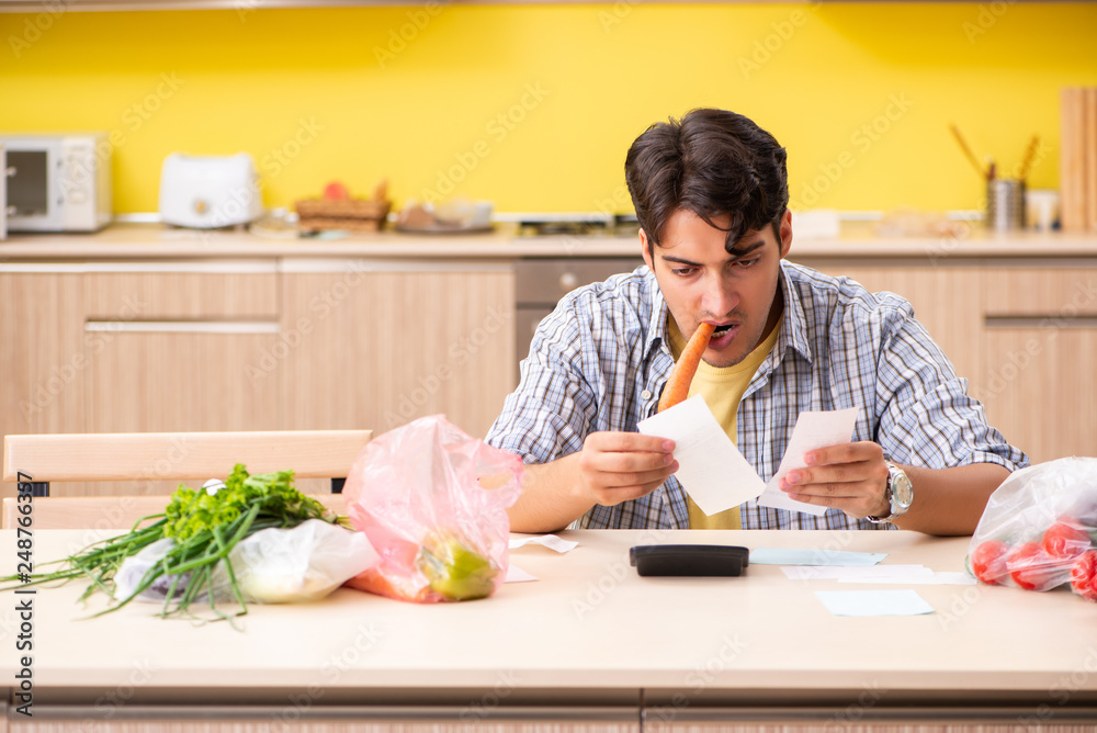 Young man calculating expences for vegetables in kitchen