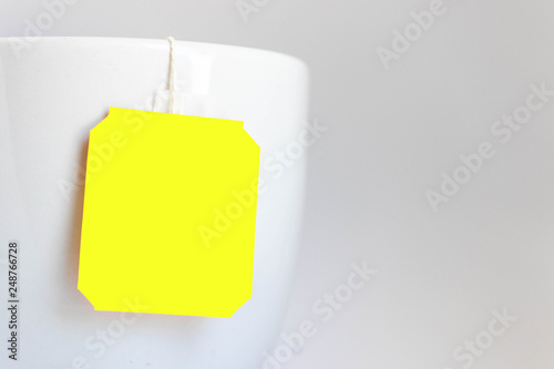 Close up of yellow label tea bag on the edge of the cup on grey background shot in studio.