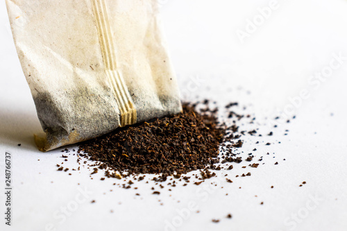 Macro close up of tea bag with dried tea leaves placed on grey background.
