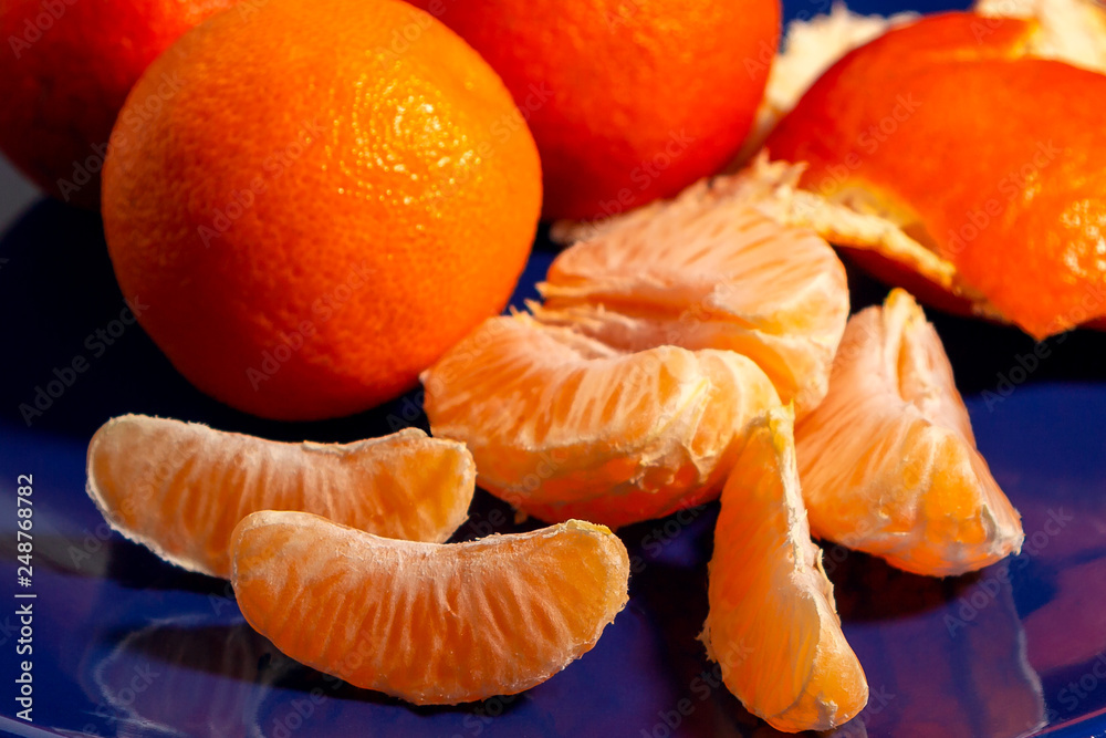 Several whole and peeled ripe tangerines on a blue plate