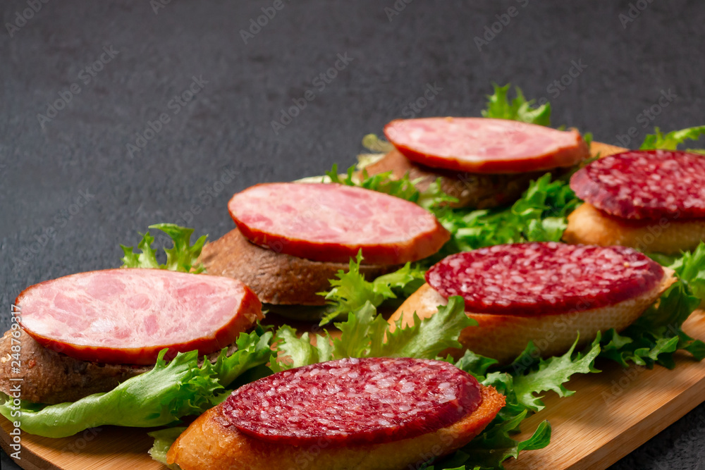 Several sandwiches with sausage and salami and sauce on a black board, background with copyspace Several sandwiches with sausage and salami and sauce on a black board, background with copyspace
