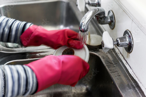 Women hand washing dishes with pink gloves on.