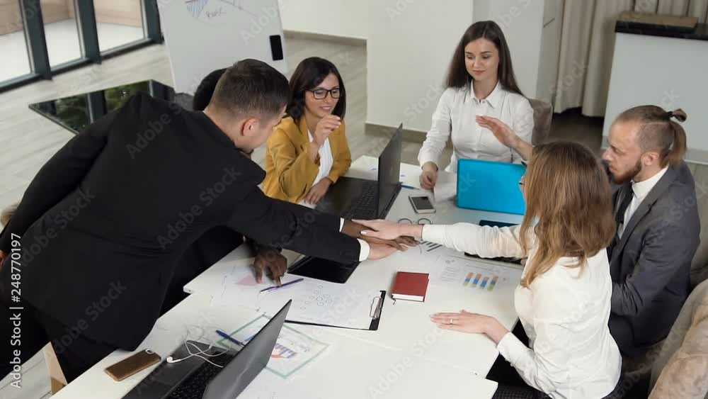 Successful business team working showing unity with their partners giving five to each other, sitting at conference table in office. Full concentration at work Successful business team working showing unity with their partners giving five to each other, sitting at conference table in office. Full concentration at work