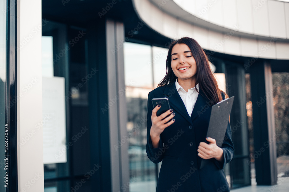 Successful smiling businesswoman or entrepreneur using phone standing in front of his office. Successful smiling businesswoman or entrepreneur using phone standing in front of his office.