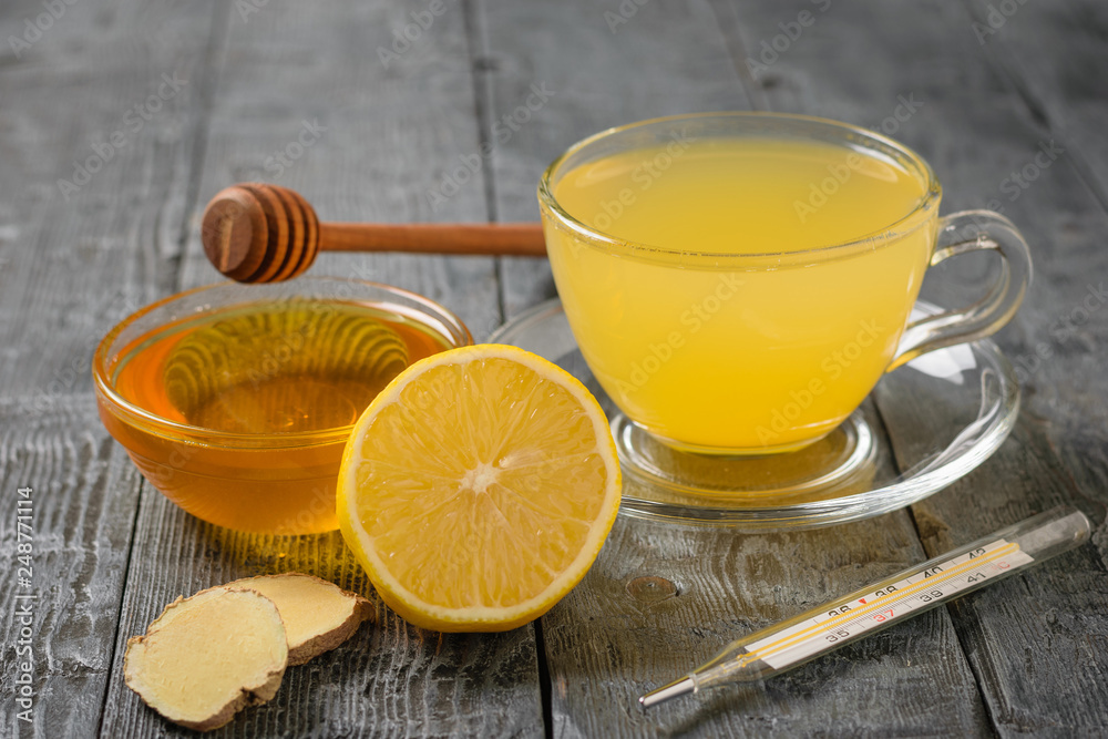 Drink ginger root, lemon, orange, honey and cinnamon and thermometer on a black wooden table. Drink ginger root, lemon, orange, honey and cinnamon and thermometer on a black wooden table.