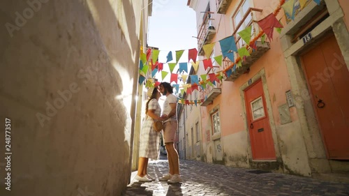 Young couple holding hands and going between buildings on narrow walkway decorated for festival in Lisbon