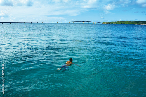 海で泳ぎながら、橋と島を見つめる男性