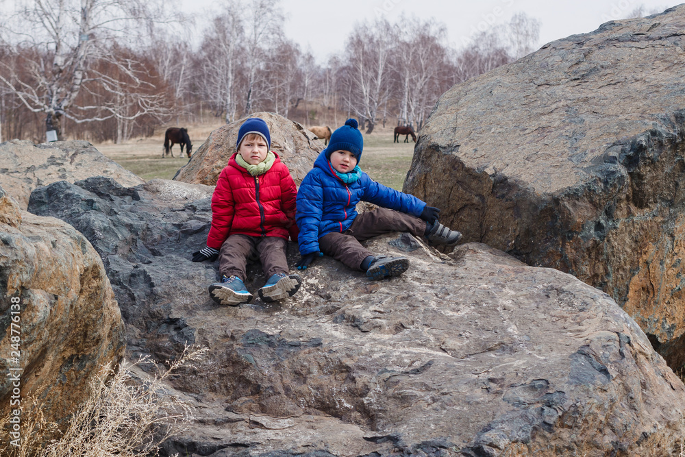 children in jackets sit on large stone