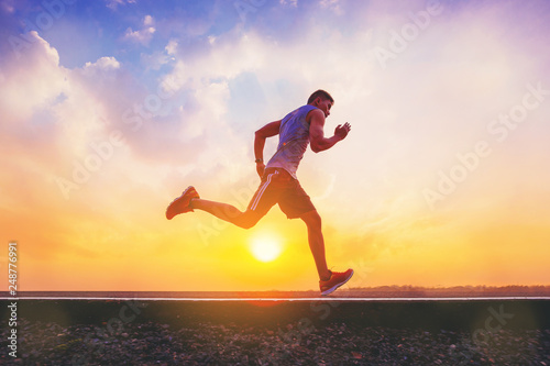 Silhouette of man running sprinting on road. Fit male fitness runner during outdoor workout with sunset background